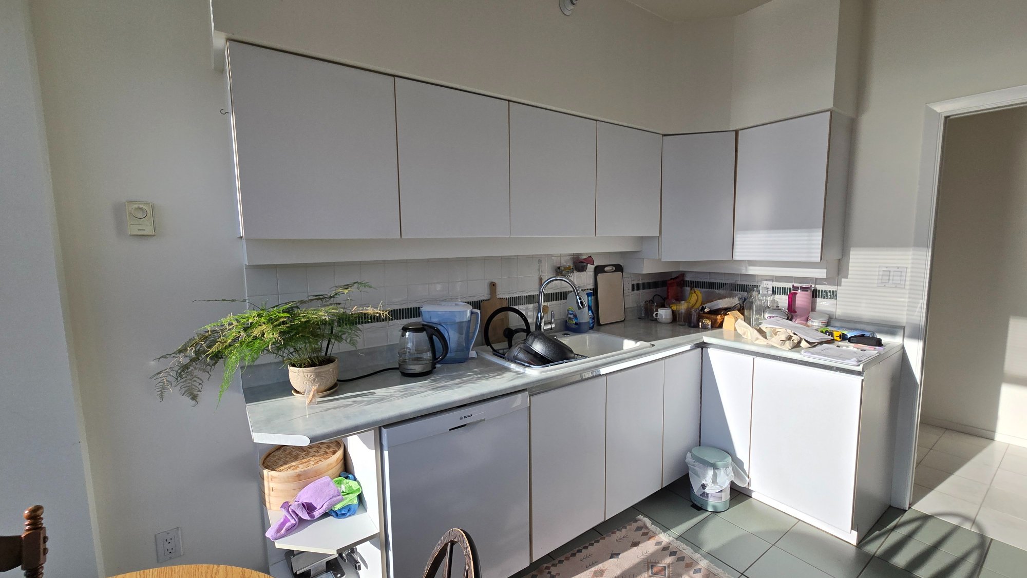 Condo kitchen before renovation — original white cabinetry and tile floor, West Vancouver