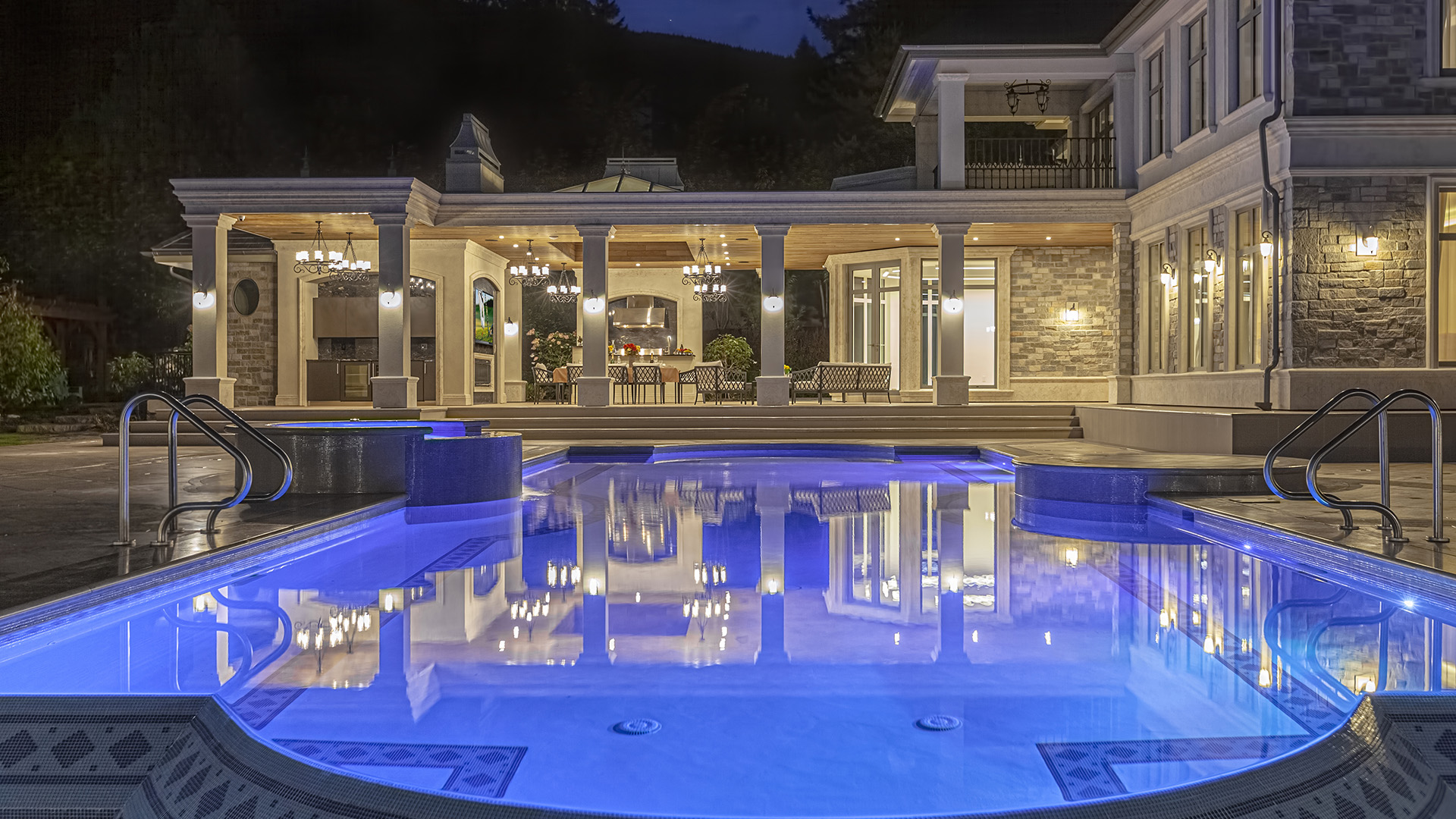 Altamont's Muse illuminated pool at night with reflections and outdoor kitchen in West Vancouver