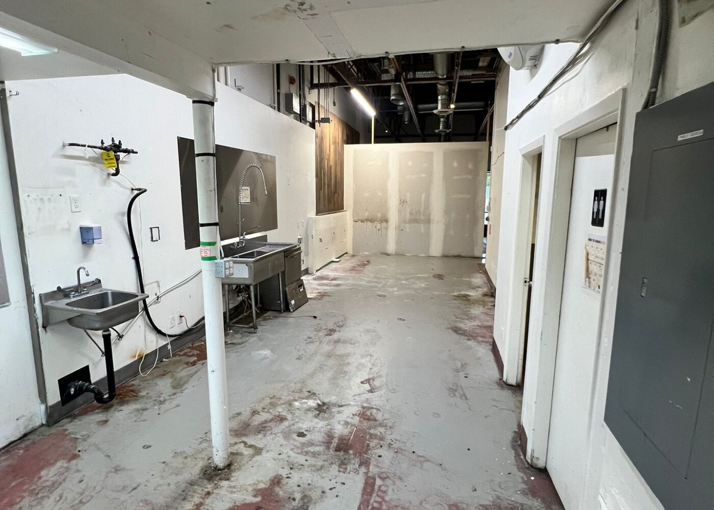 Back area during demolition with exposed utilities, removed cabinetry, and stripped walls in commercial restoration