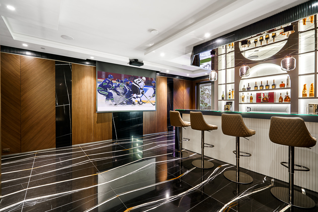 Entertainment bar with nero marquina black marble floor quilted leather stools projection screen and backlit spirits shelving West Vancouver
