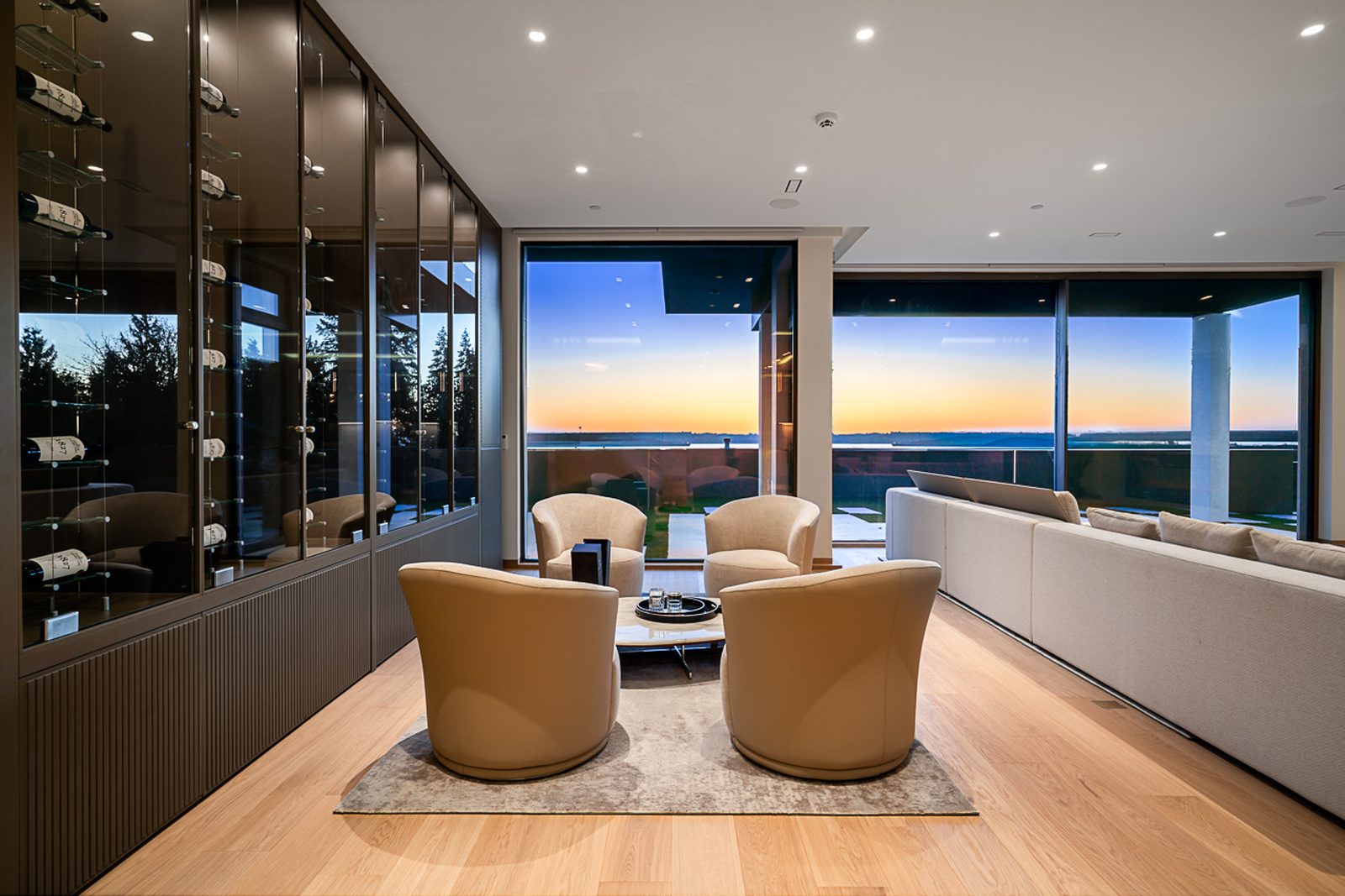 Lounge with swivel chairs glass wine display cabinets and sunset ocean view Altamont West Vancouver estate
