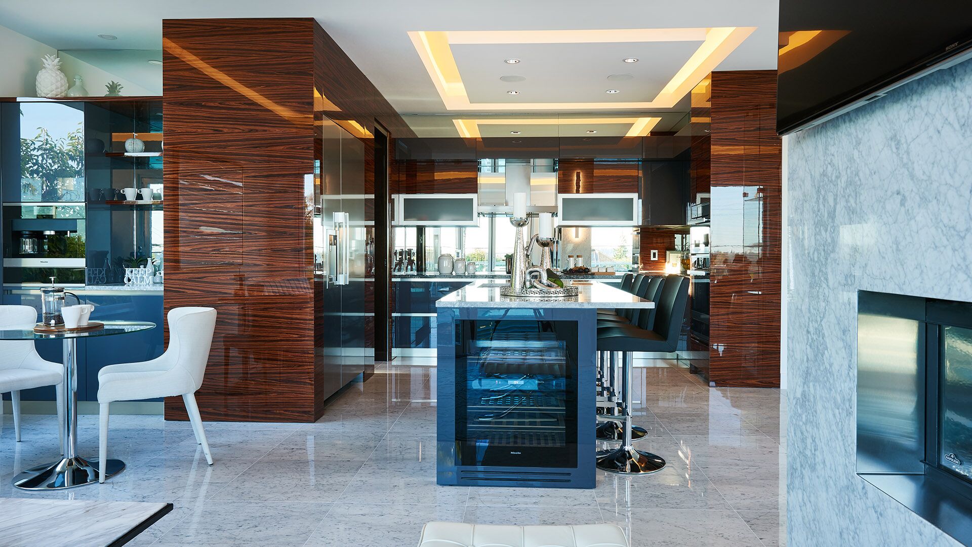 Kitchen living area with Miele wine fridge island marble fireplace wall zebrawood columns and breakfast nook at California Dreams designed and installed by Eurohouse Construction