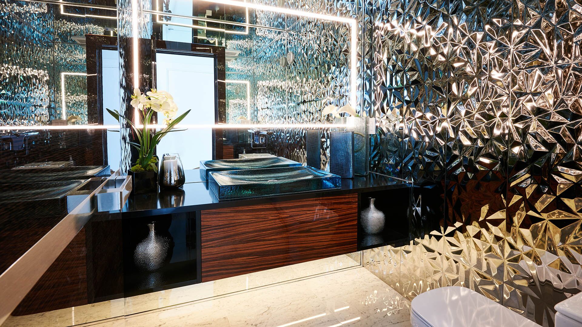 Luxury powder room with floor-to-ceiling faceted metallic chrome tile walls sculpted glass vessel sink zebrawood floating vanity and LED-framed mirror at California Dreams designed and installed by Eurohouse Construction