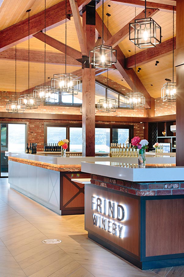 Frind Estate Winery completed tasting bar — illuminated signage, exposed timber trusses, brick walls, and geometric pendant lighting — designed by Eurohouse Studio