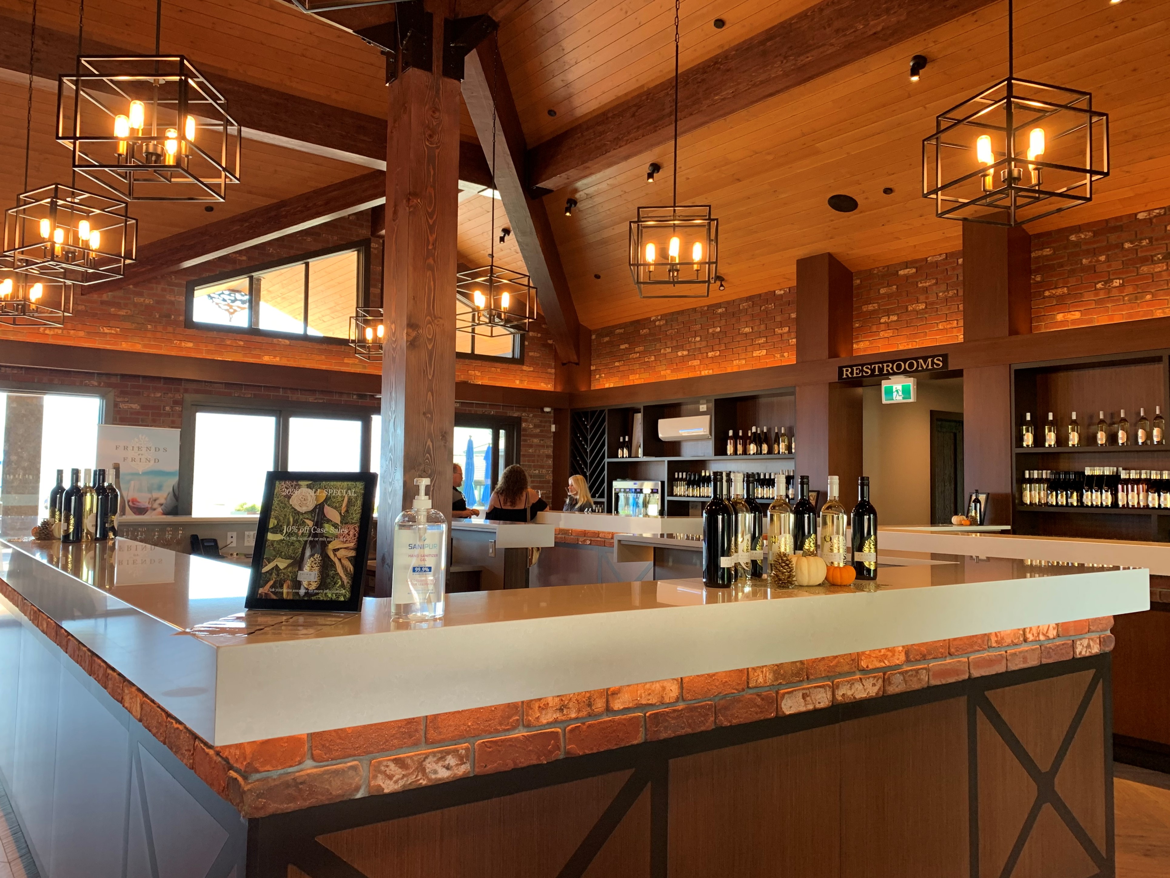 Frind Estate Winery tasting bar in operation — stone countertops, wine displays, exposed cedar ceiling, and brick feature walls — designed by Eurohouse Studio