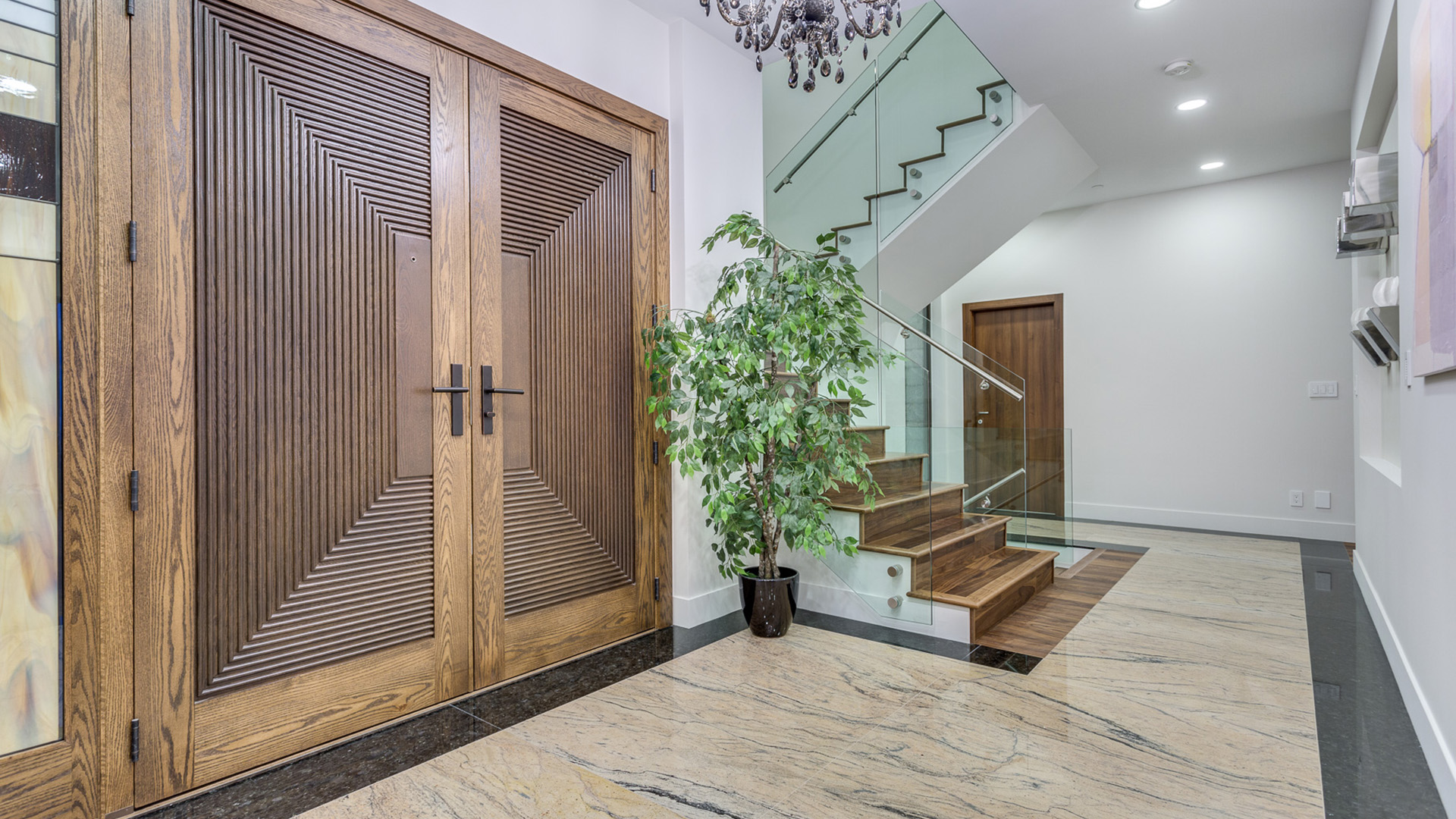 Grand entrance foyer with custom carved oak double doors polished marble floors floating walnut staircase glass railings and crystal chandelier Millstream British Properties West Vancouver