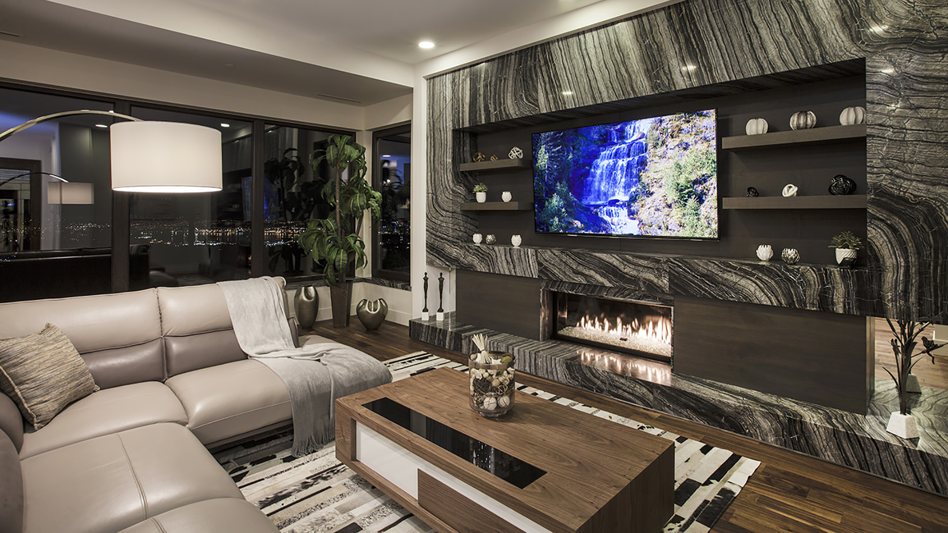 Lower level family room with dramatic dark marble feature wall integrated linear fireplace floating walnut shelves and panoramic city views Millstream British Properties
