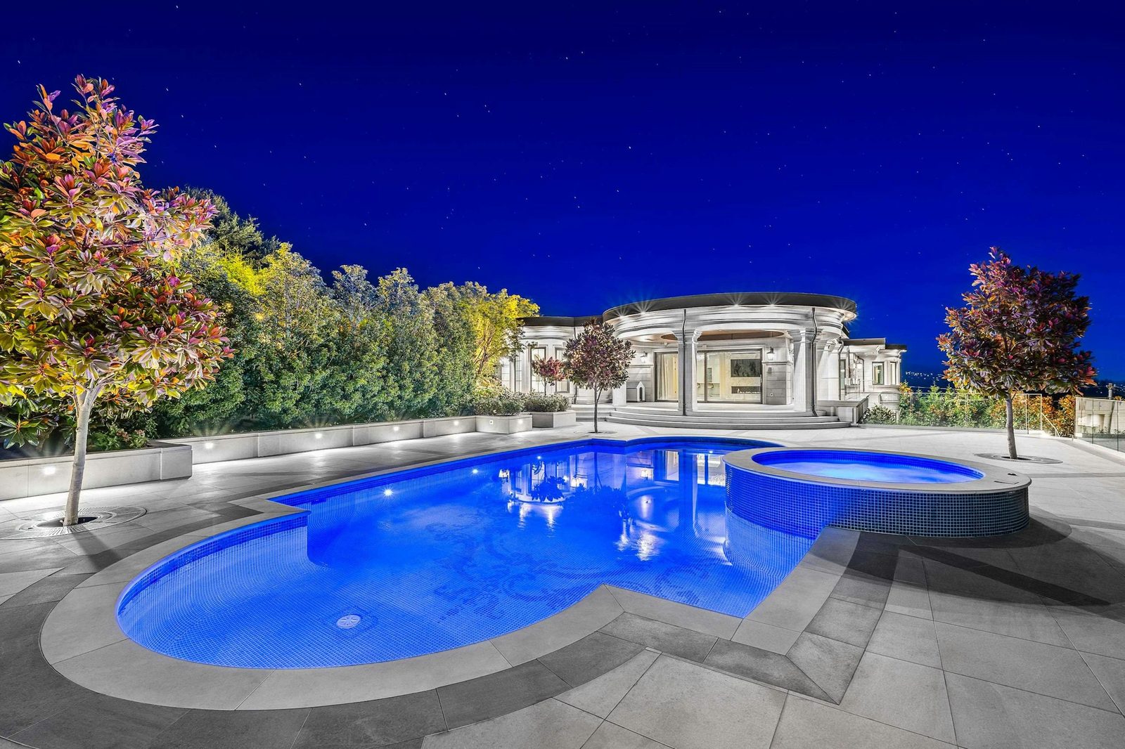 Pool terrace and limestone residence illuminated at night in West Vancouver
