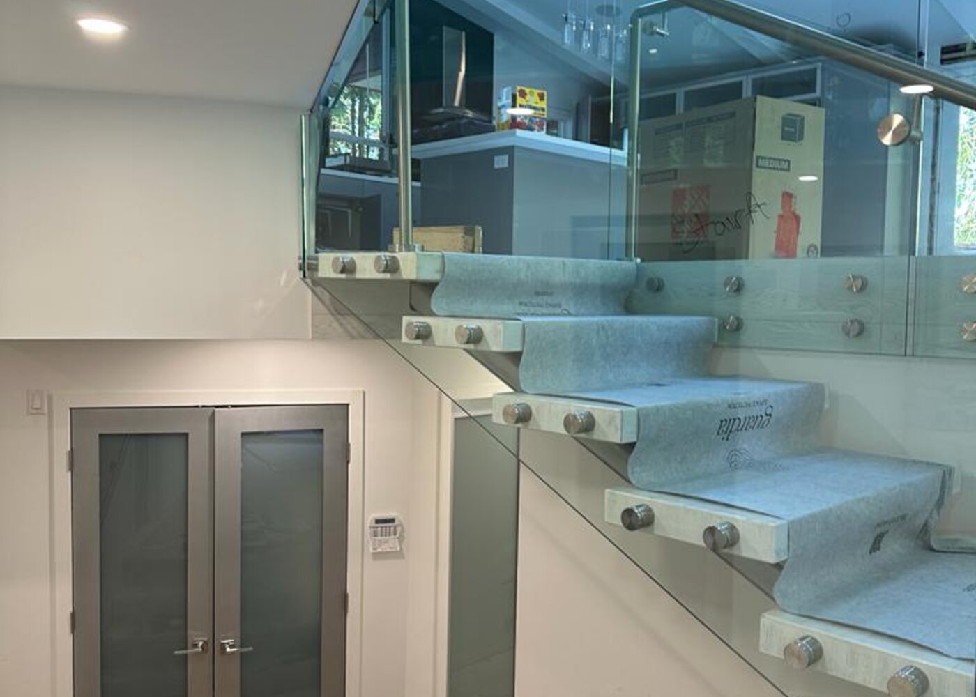 Floating staircase with glass railing viewed from below showing entry level with double doors and marble floor tiles