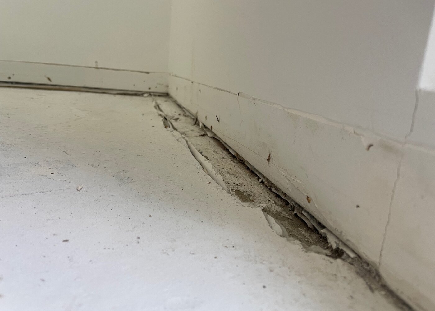 Large gap between subfloor and baseboard revealing deteriorated concrete and missing material at wall junction