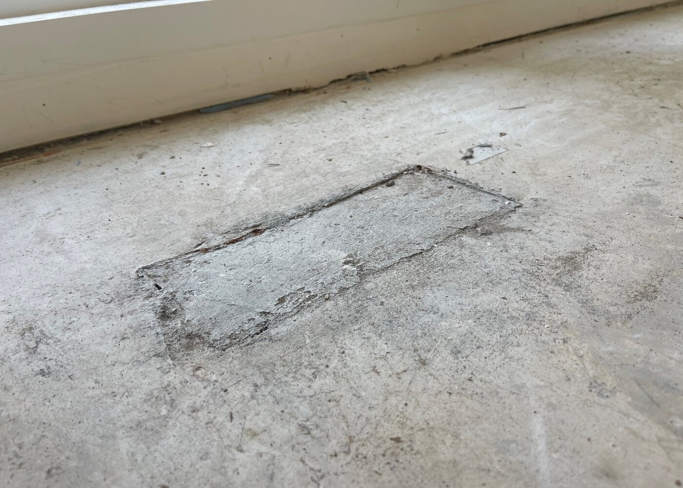Patched hole in concrete subfloor showing prior repair attempt that failed to create a level surface for flooring installation
