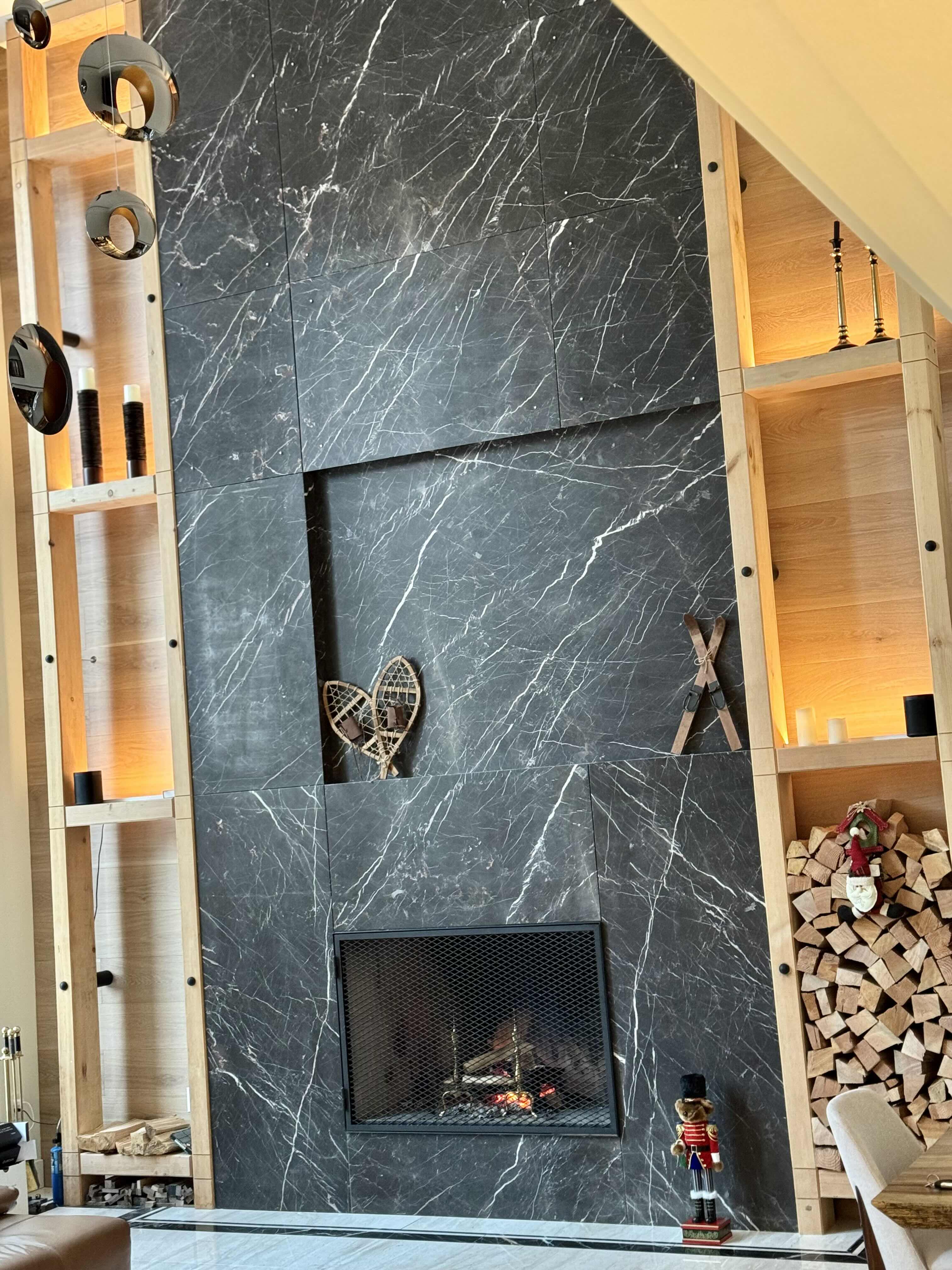 Double-height Italian marble fireplace feature wall with oak shelving, backlit display niches, and firewood storage at Rainbow in Whistler luxury custom home by Eurohouse Construction