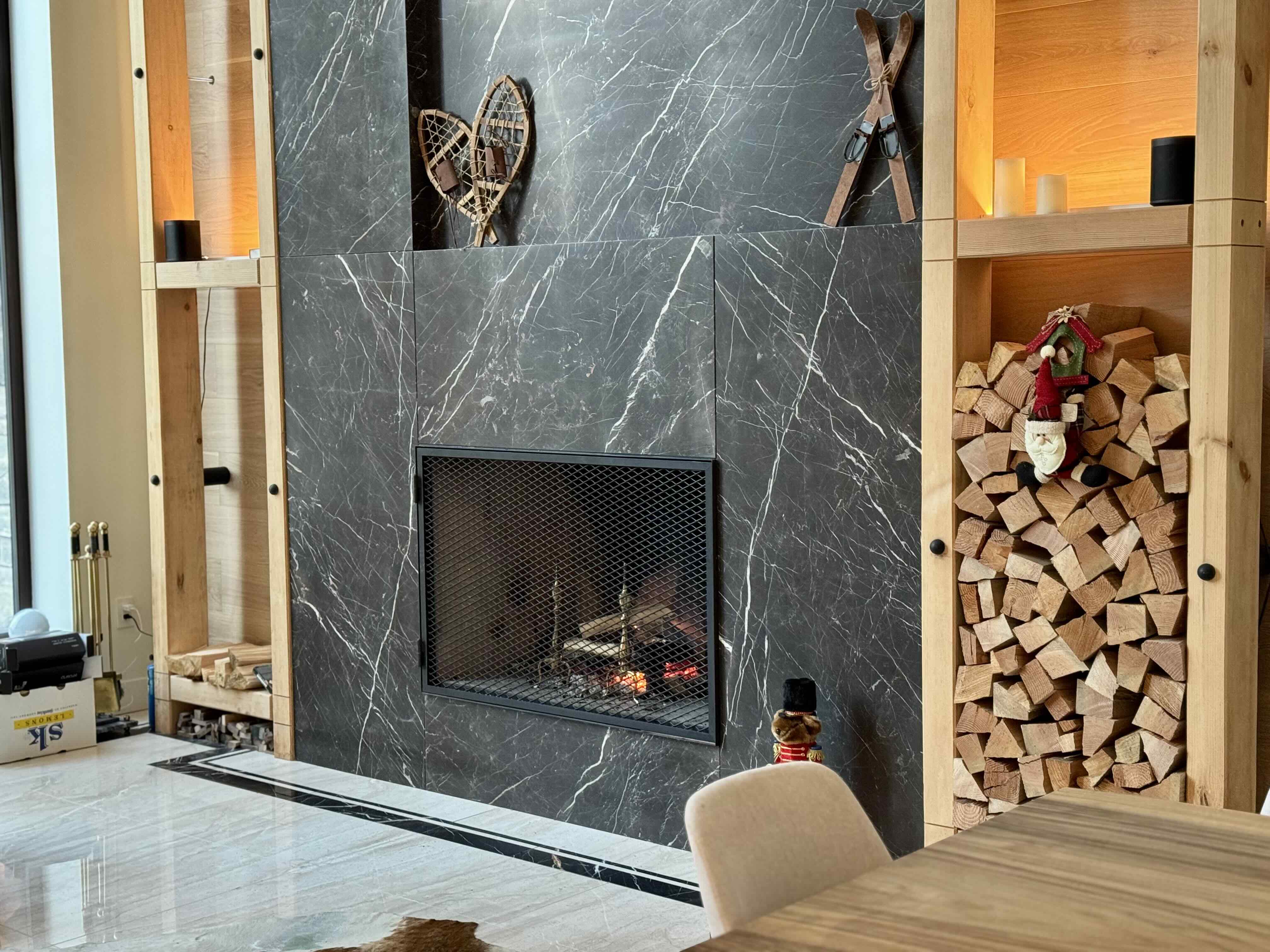 Italian marble fireplace with integrated firewood storage, snowshoe and ski displays, and backlit oak shelving at Rainbow in Whistler by Eurohouse Construction