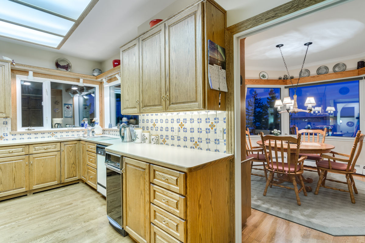 Original kitchen before renovation with oak cabinetry patterned tile backsplash fluorescent ceiling lights terra cotta tile floor and arched doorway at Rockridge Classic before Eurohouse Construction renovation