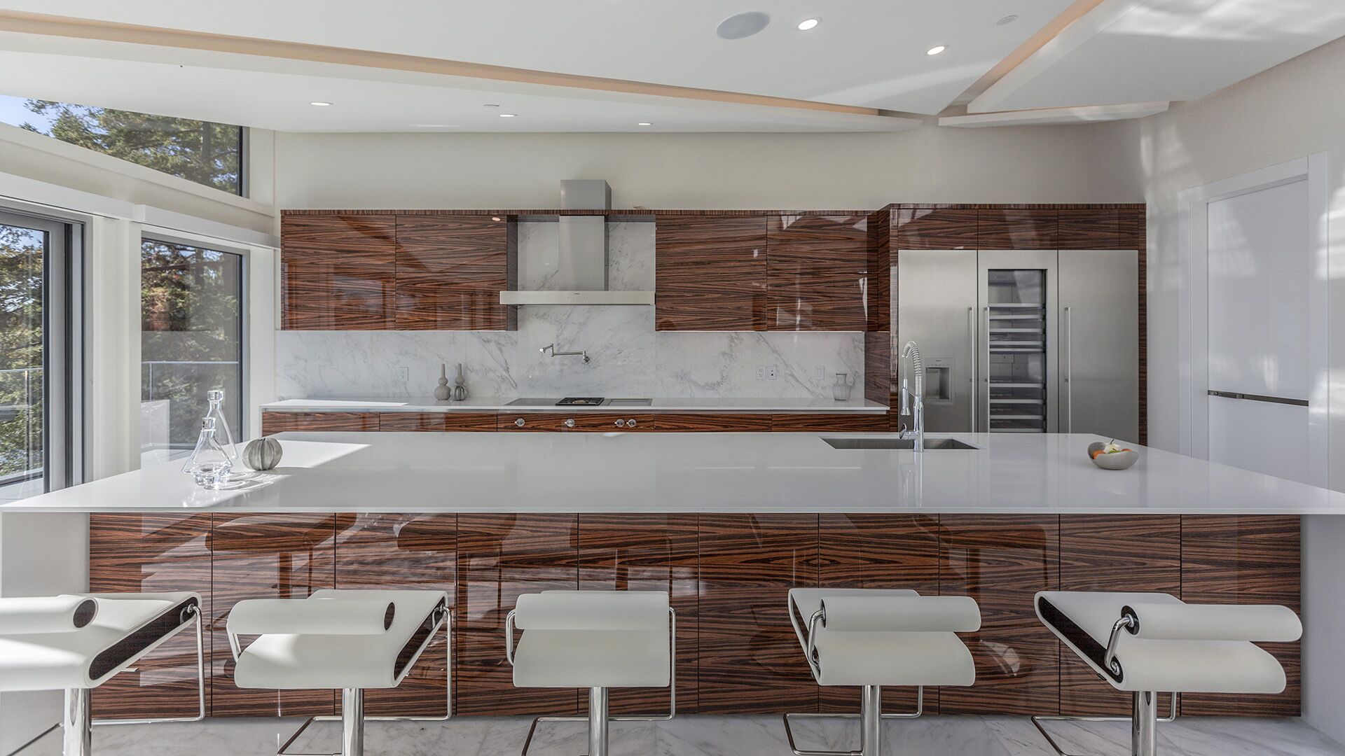 Front view of luxury zebrawood kitchen with bar seating white quartz countertop and professional stainless appliances at The Riva Club designed and installed by Eurohouse Construction