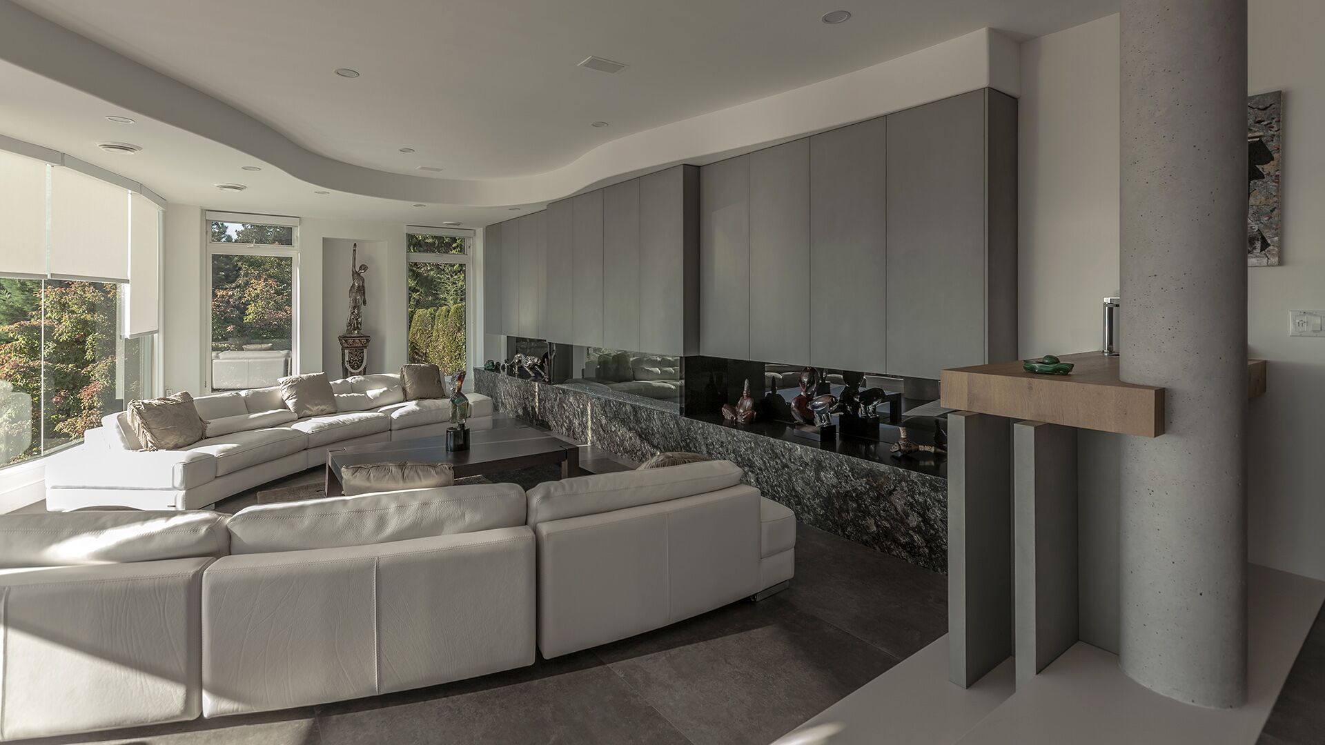 Living room angle showing white leather sectional natural granite stone console with art objects smoked mirror Italian cabinetry and concrete column at The Zen on Bramwell renovated by Eurohouse Construction