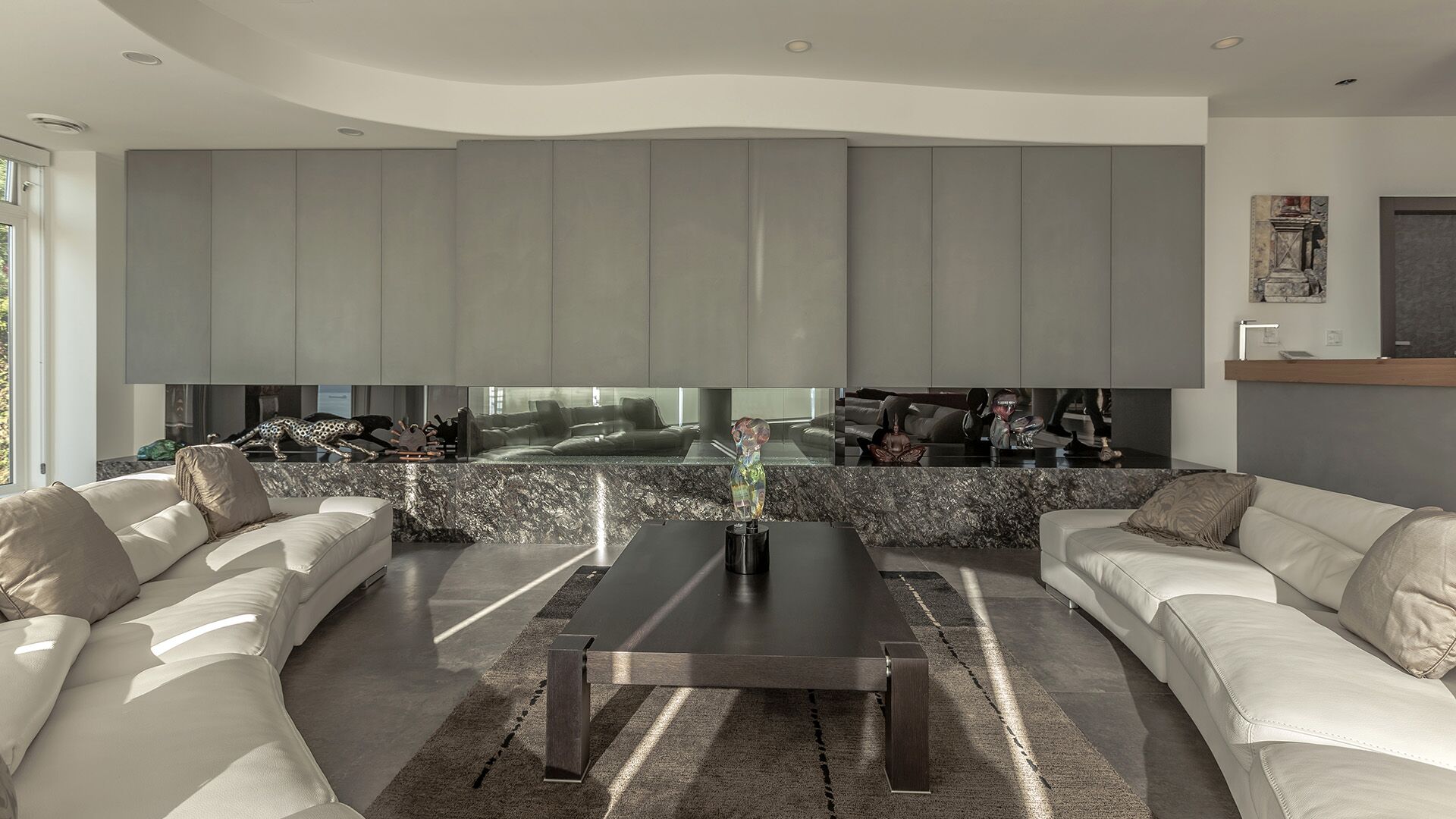 Living room with twin white leather sofas natural granite stone media wall smoked mirror backsplash Italian grey matte cabinetry and sculptured ceiling at The Zen on Bramwell renovated by Eurohouse Construction