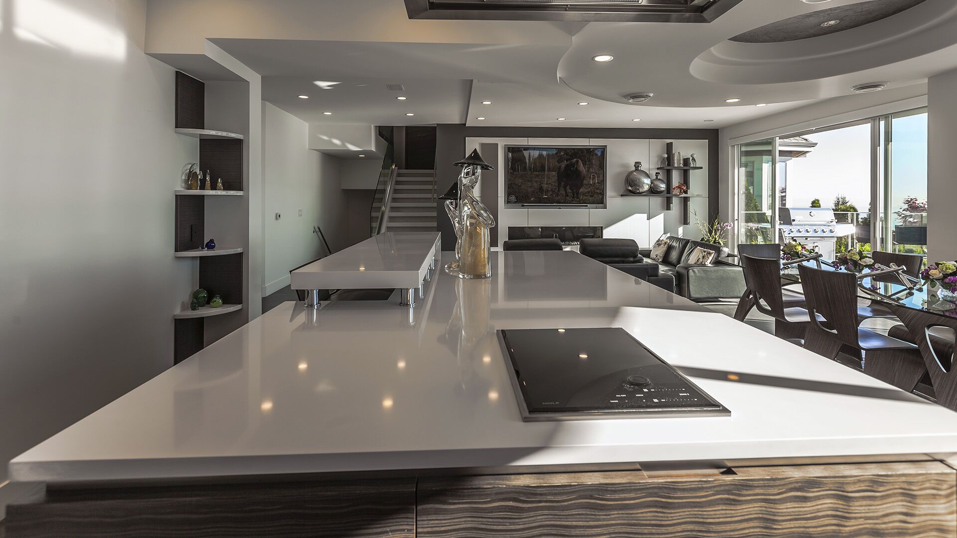 Kitchen island with Wolf induction cooktop white quartz counter looking toward living room media wall glass staircase and ocean view terrace at The Zen on Bramwell renovated by Eurohouse Construction
