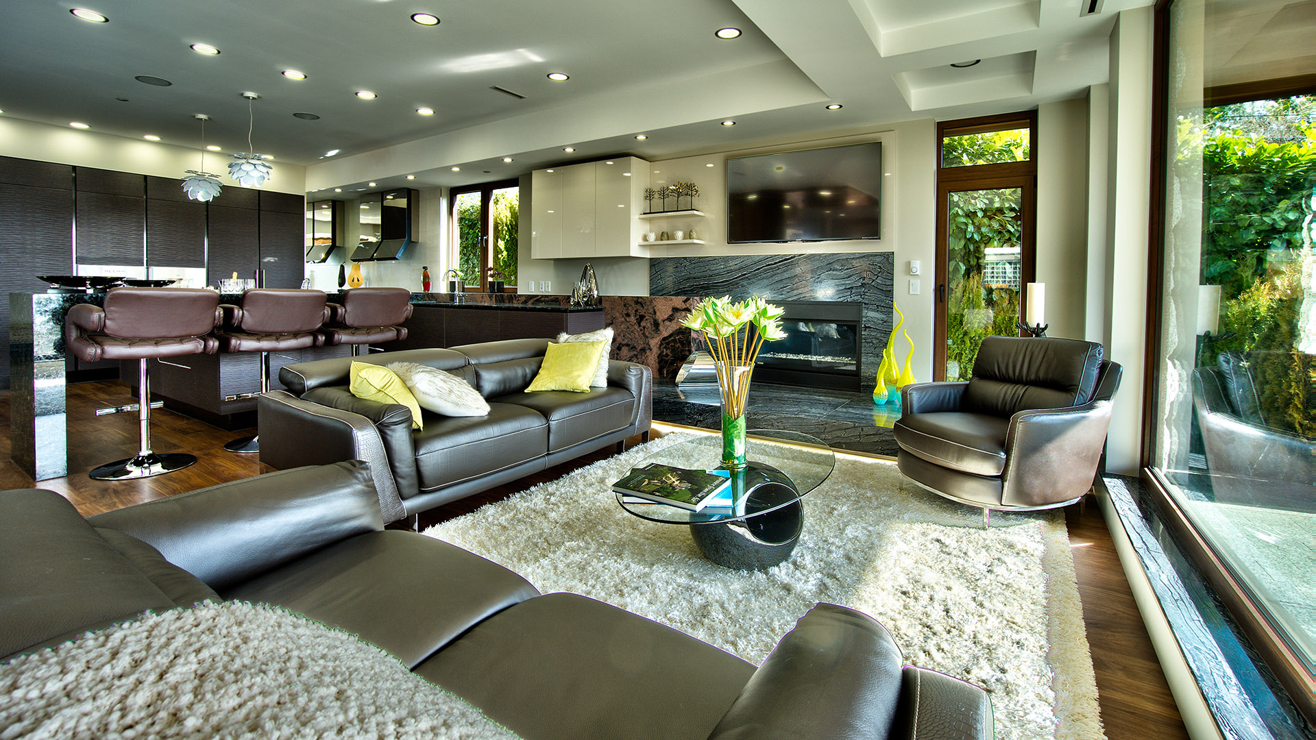 Open-plan living room with marble slab fireplace leather sectional and floor-to-ceiling windows leading to pool deck West Bay West Vancouver