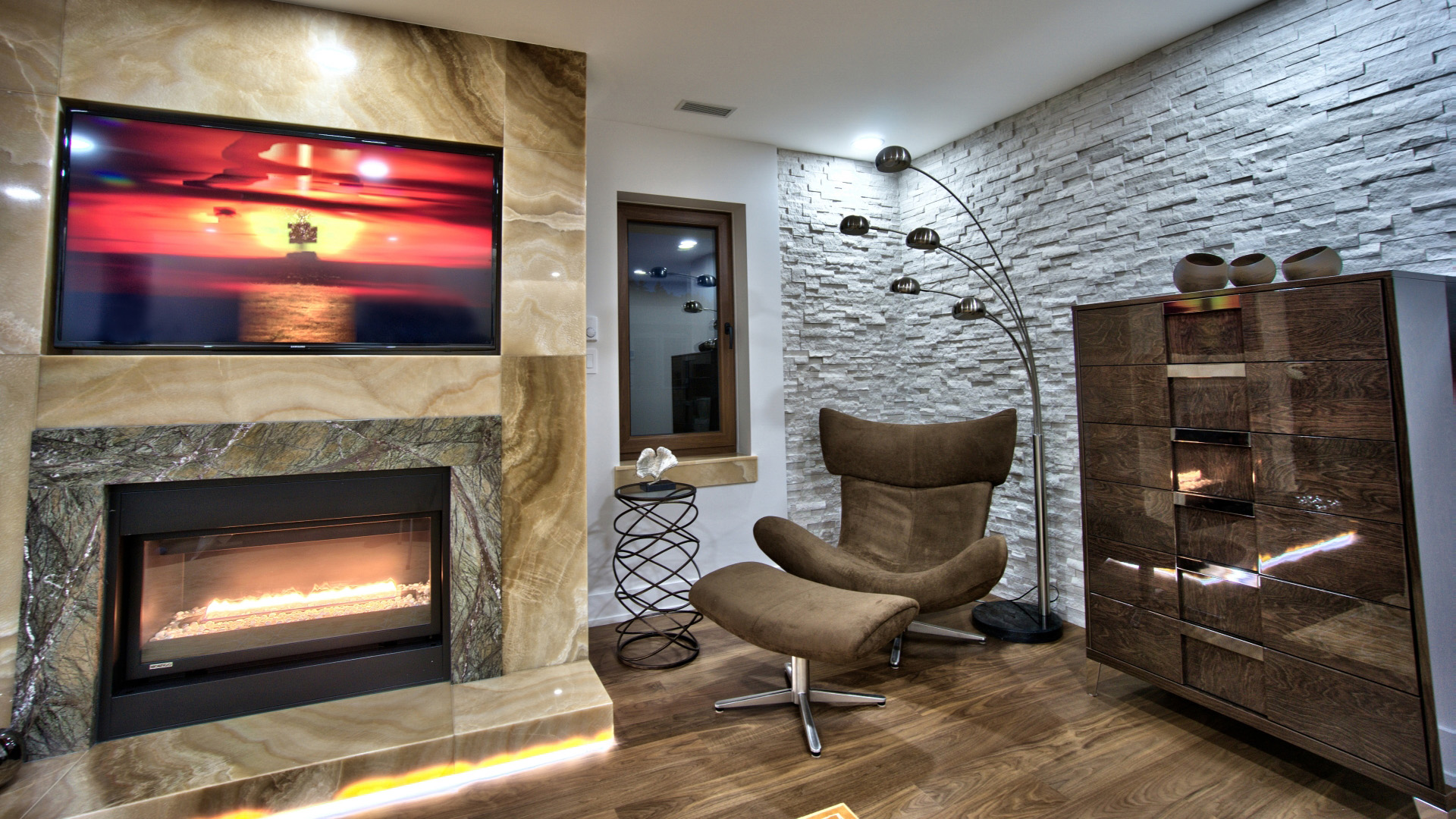 Private lounge with backlit onyx fireplace surround stacked stone accent wall and designer armchair West Bay West Vancouver