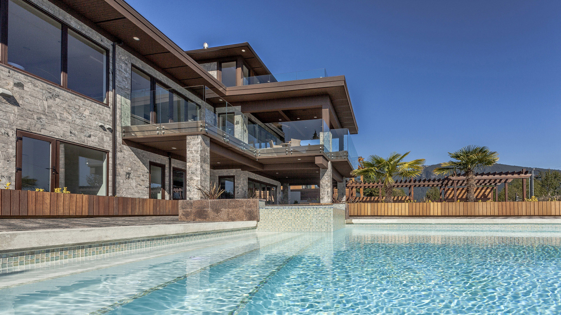 Pool level view of West Coast Contemporary showing swimming pool Italian glass-tiled hot tub granite facade timber pergola and glass railings British Properties West Vancouver