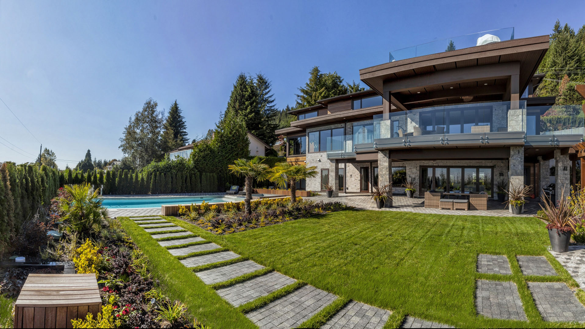 Rear garden view of West Coast Contemporary showing landscaped lawn granite stepping stones pool terrace timber pergola and glass railings British Properties West Vancouver