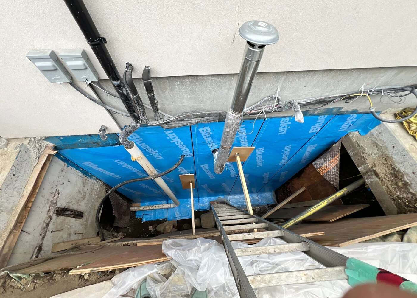 Overhead view of completed Blueskin waterproofing membrane installation on foundation wall with utility penetrations