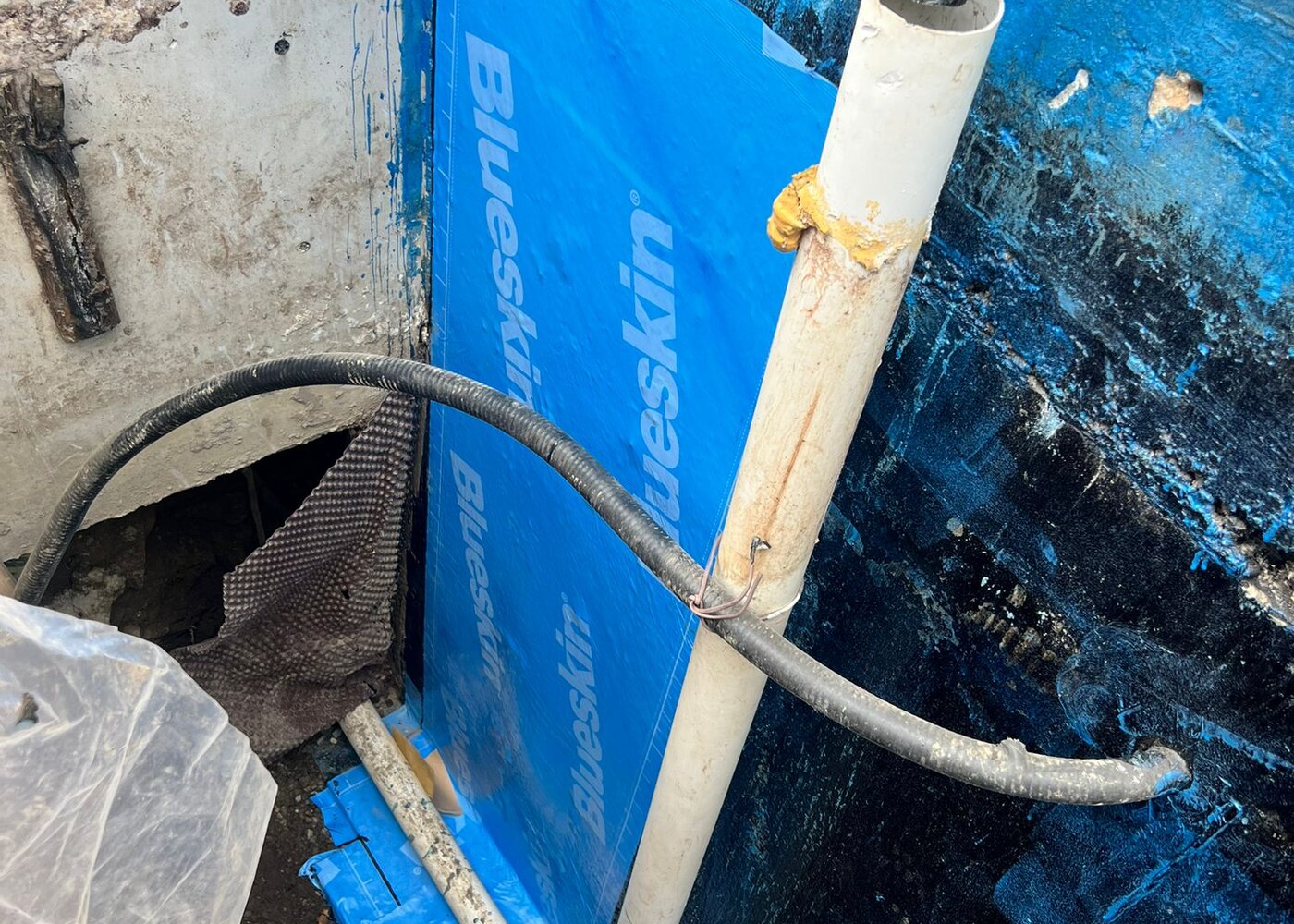 Blueskin membrane sealed around pipe penetrations through foundation wall with proper lapping and adhesion