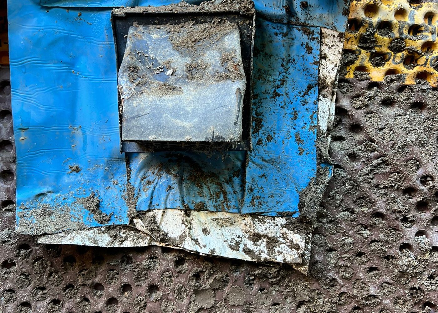 Close-up of failed waterproofing membrane with blue tape and deteriorated dimple board removed from foundation wall