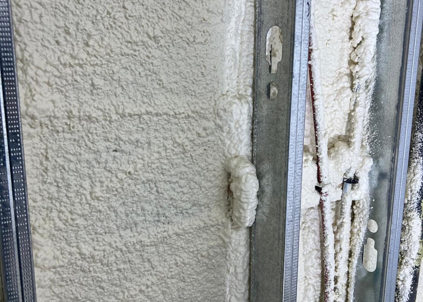 Closed-cell spray foam insulation applied to steel stud wall against concrete foundation for moisture and thermal barrier